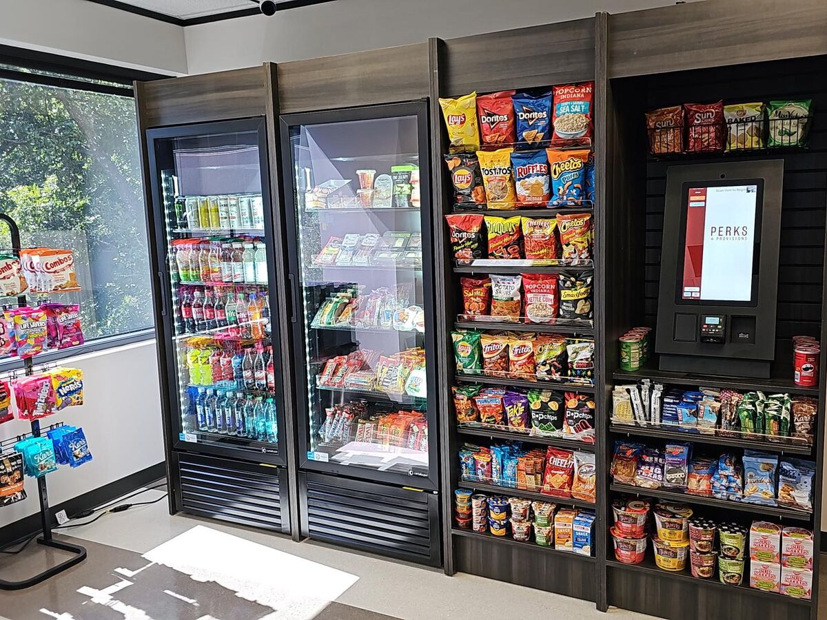 A Perks + Provisions micro market: glass-door coolers, a full snack wall, and a self-checkout kiosk
