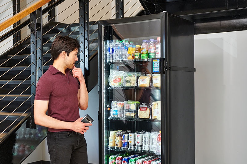 An employee choosing a drink from a stocked AI smart cooler in an office